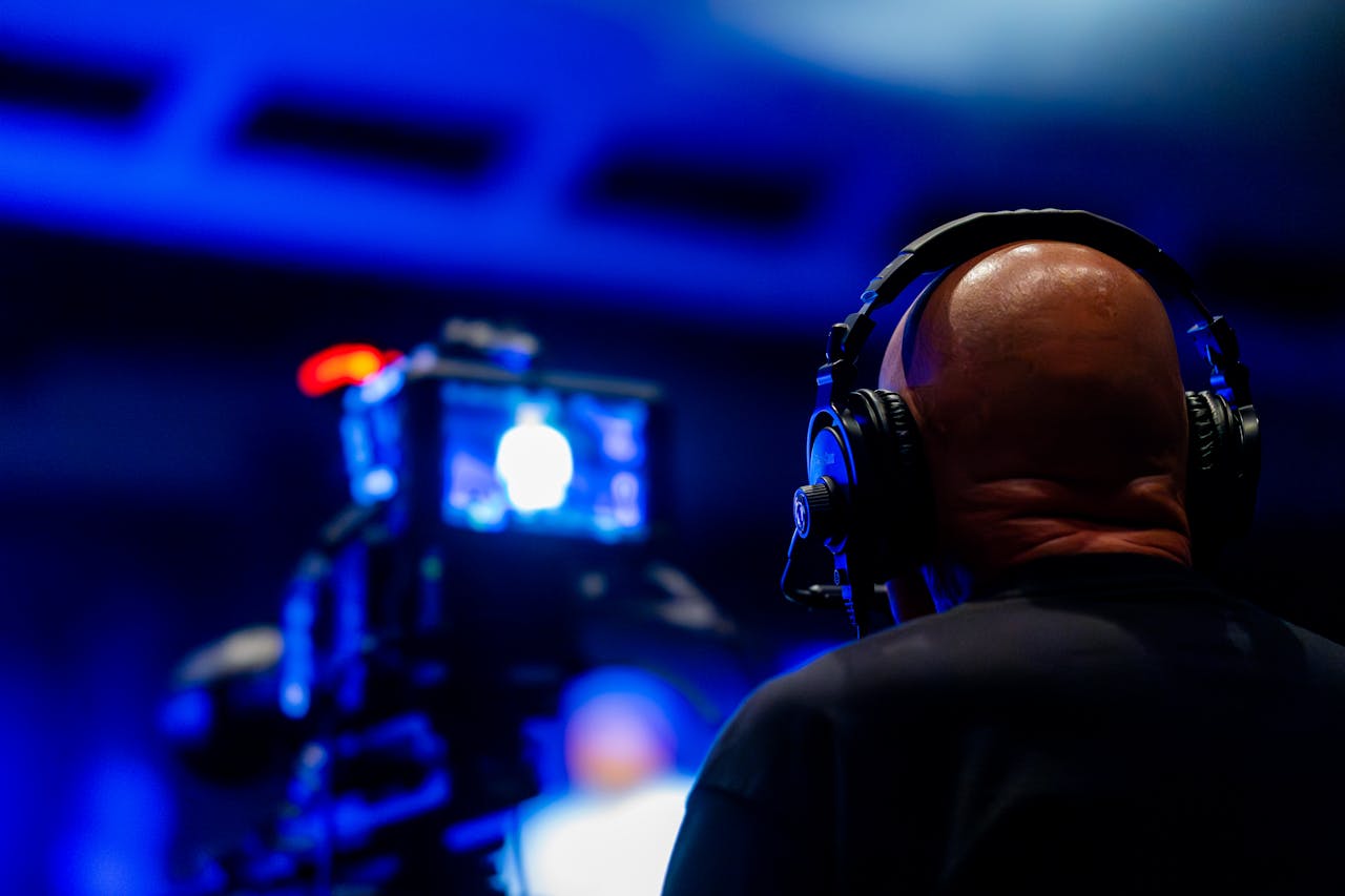 A videographer wearing headphones captures an event with professional video equipment in a dimly lit setting.